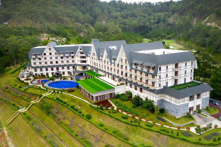 Aerial view of a grand hotel with well-manicured gardens nestled in a forest setting.